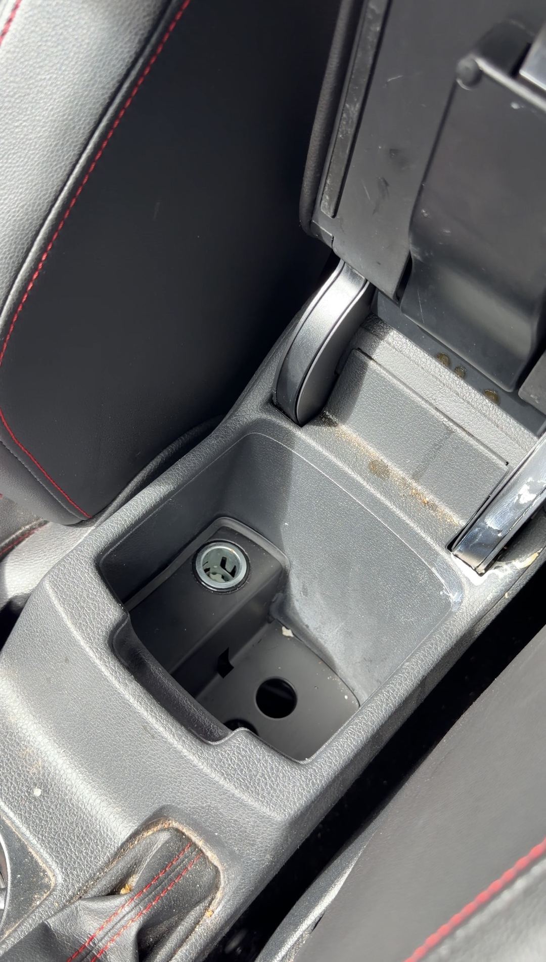 Open armrest storage bin of a VW GTI with crumbs and dust before cleaning