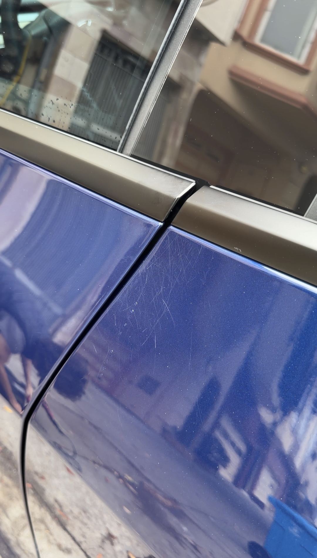 Close-up of fine scratches and dried water spots on the door of a deep blue Tesla Model Y before detailing.