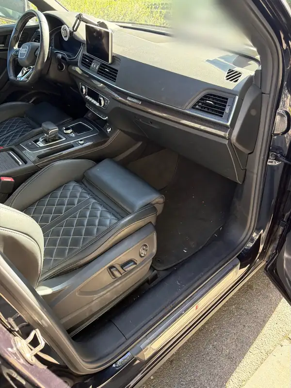 Front passenger footwell of an Audi SQ5 before detailing, with crumbs and dirt on the carpet and sill