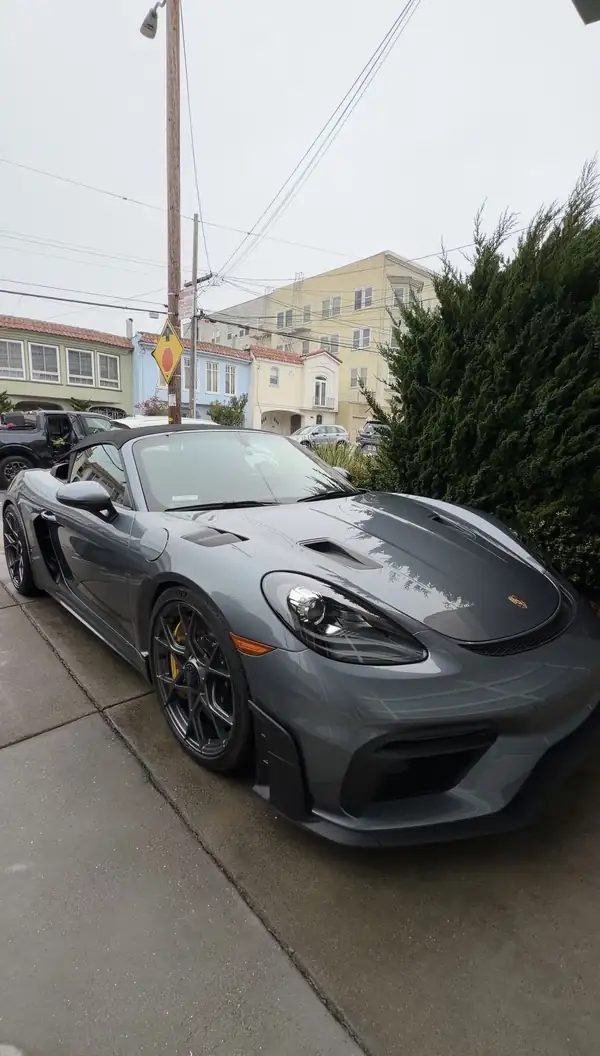 Clean grey Porsche 718 Spyder RS with its black soft top up, parked on a San Francisco driveway after a mobile detail.