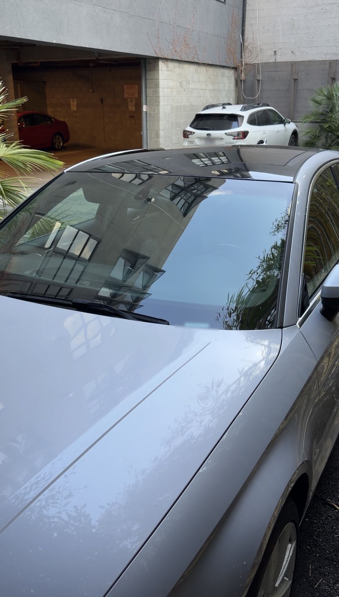 Hood and windshield of a silver Audi A3 reflecting nearby buildings