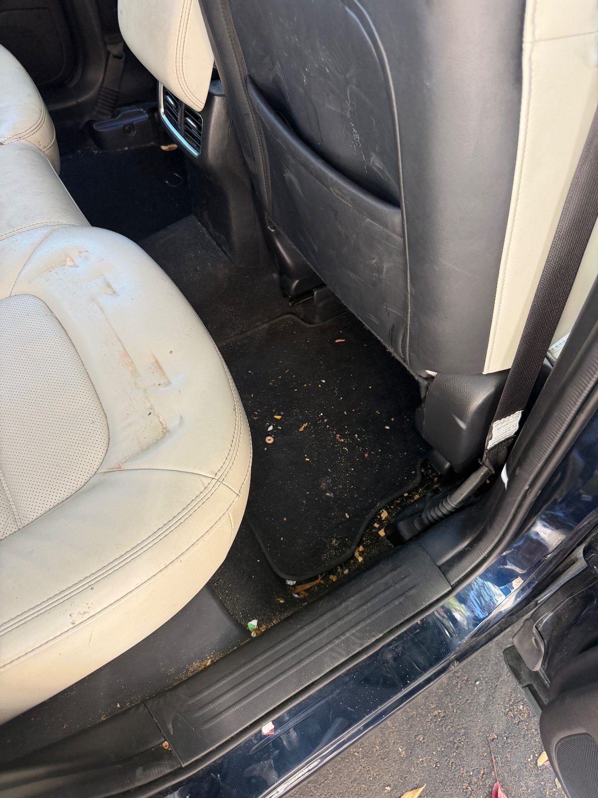 Rear footwell of a dark blue Mazda CX-5 before detailing, mat covered in crumbs and the cushion stained