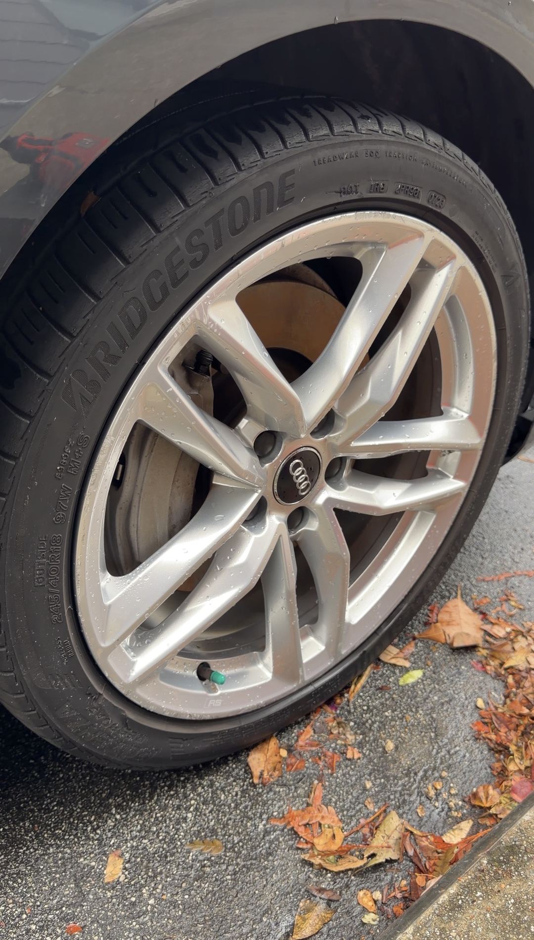 Clean, wet twin five-spoke front alloy wheel of a grey Audi A4 with a Bridgestone tyre