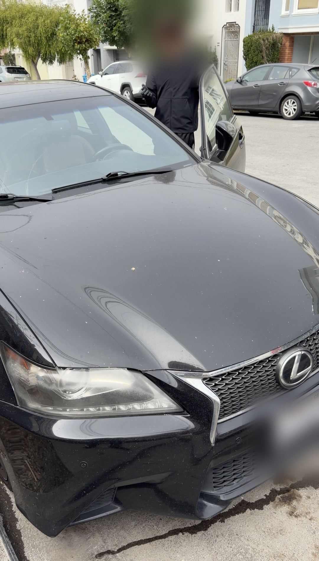 Black Lexus GS with a dusty, water-spotted hood parked on a San Francisco street before detailing, driver's door open.