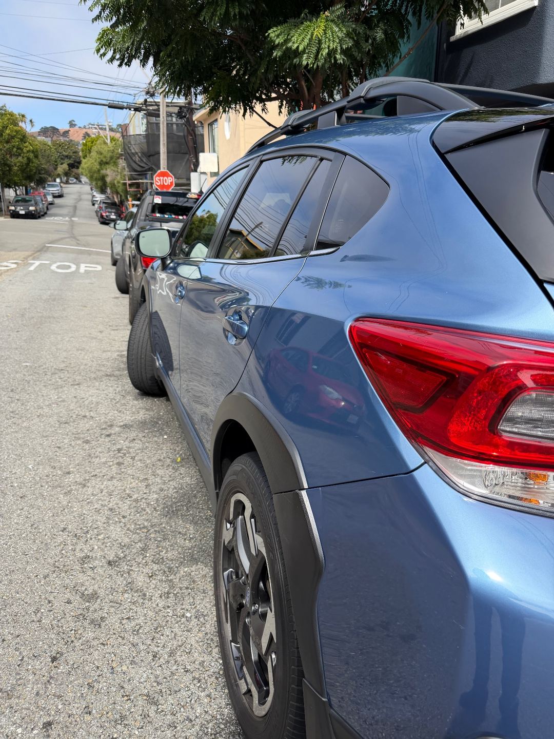 Rear quarter of a blue Subaru Crosstrek after washing, glossy paint reflecting the street