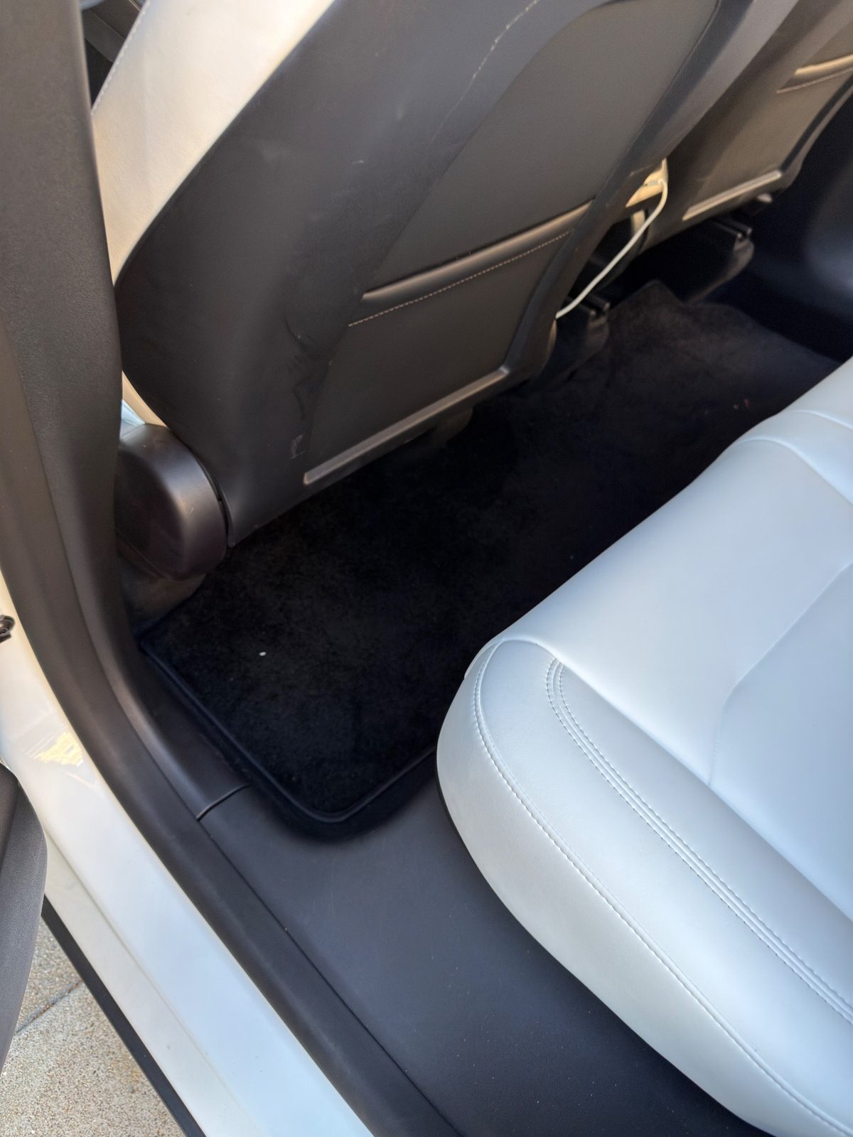 Rear driver-side footwell and seatback of a white Tesla Model Y before detailing, with a dirt smear on the seatback panel