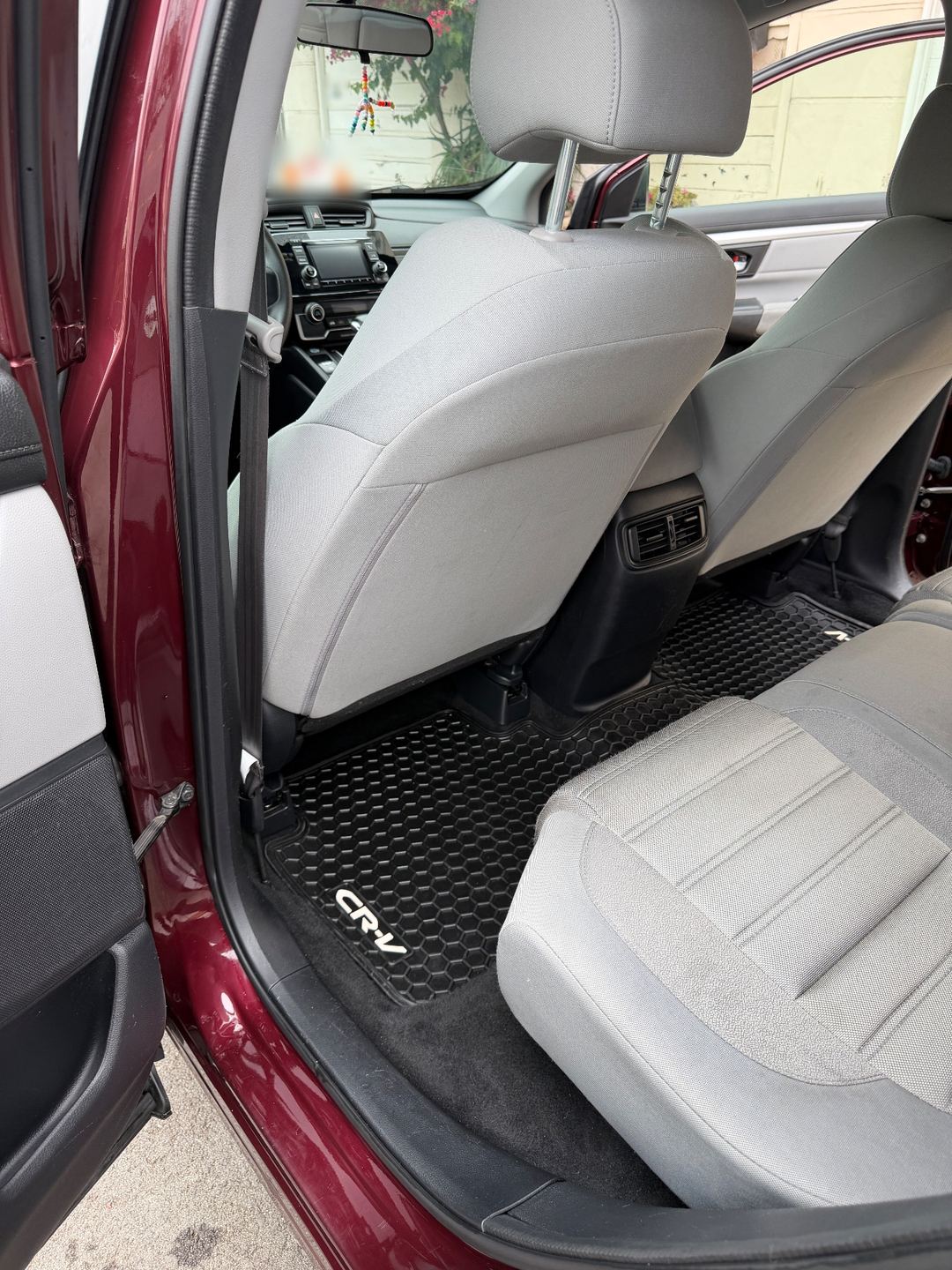 Rear footwell of a maroon Honda CR-V after detailing, a clean black rubber mat and clean grey cloth seat