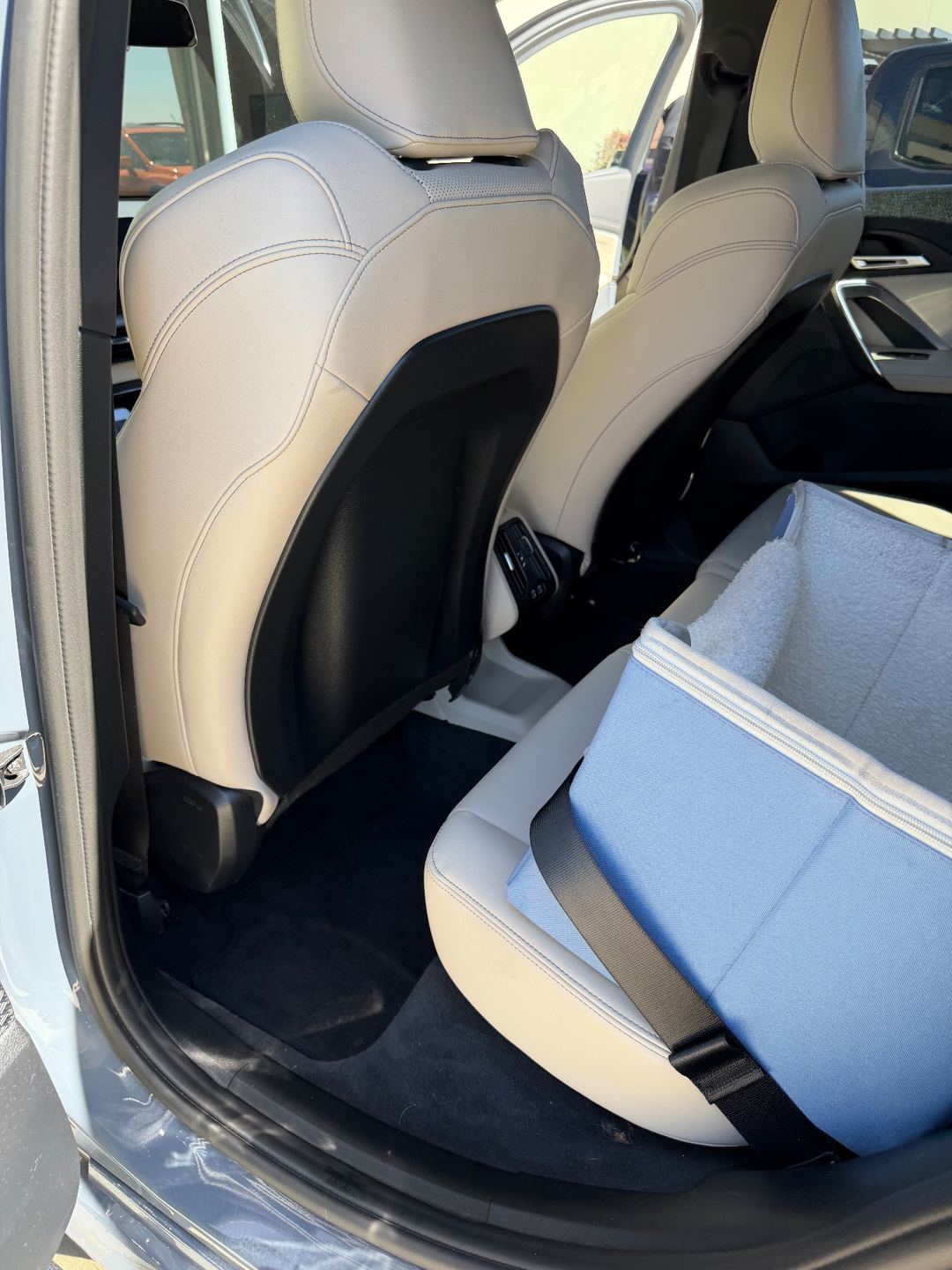 Rear driver-side footwell of a grey BMW X1 before detailing, with a pet booster seat on the bench and lint on the carpet
