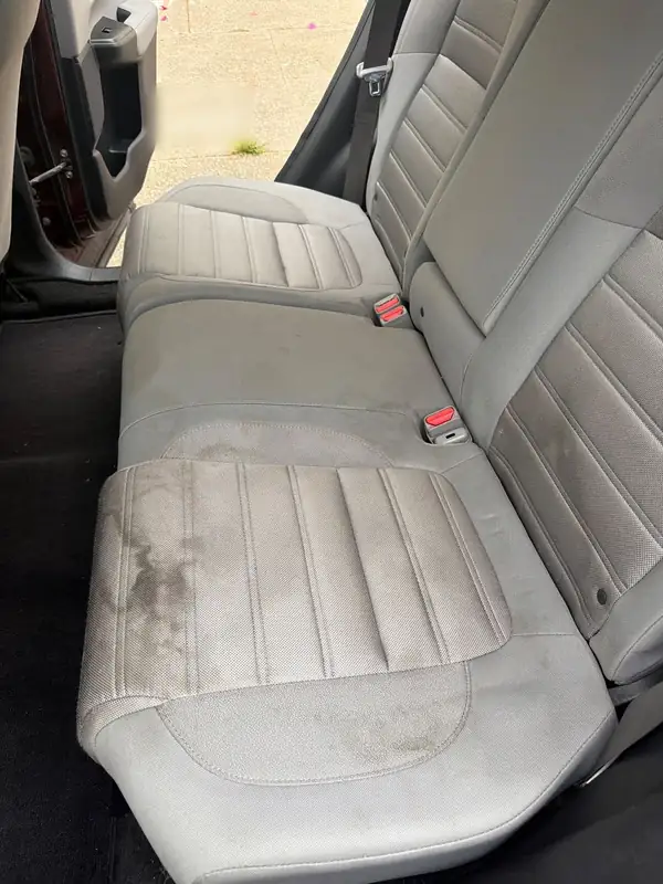 Rear bench of a maroon Honda CR-V before detailing, the grey cloth cushion covered in large dark stains