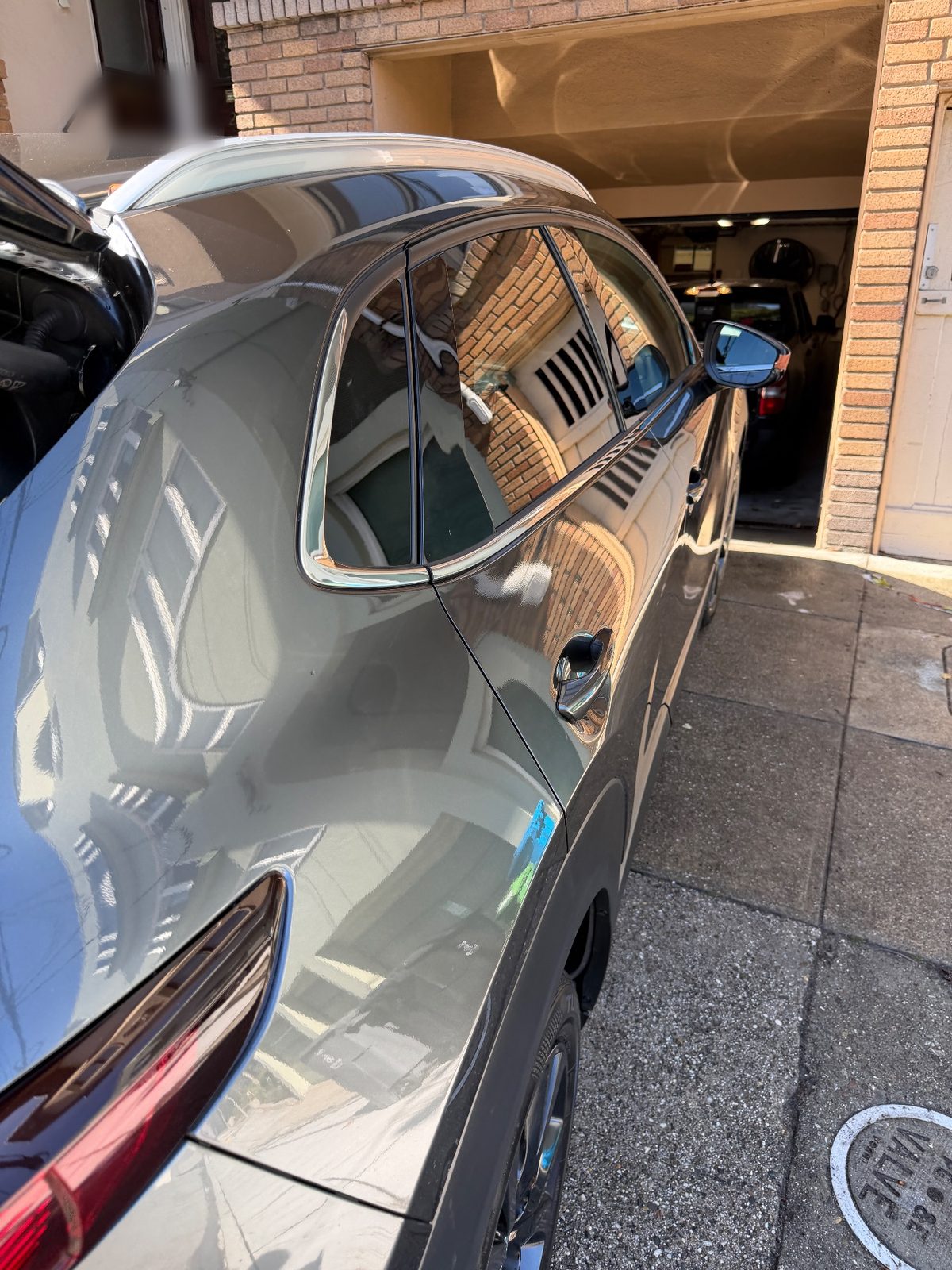 Rear quarter of a grey Mazda CX-30 after the wash, glossy paint reflecting a brick house