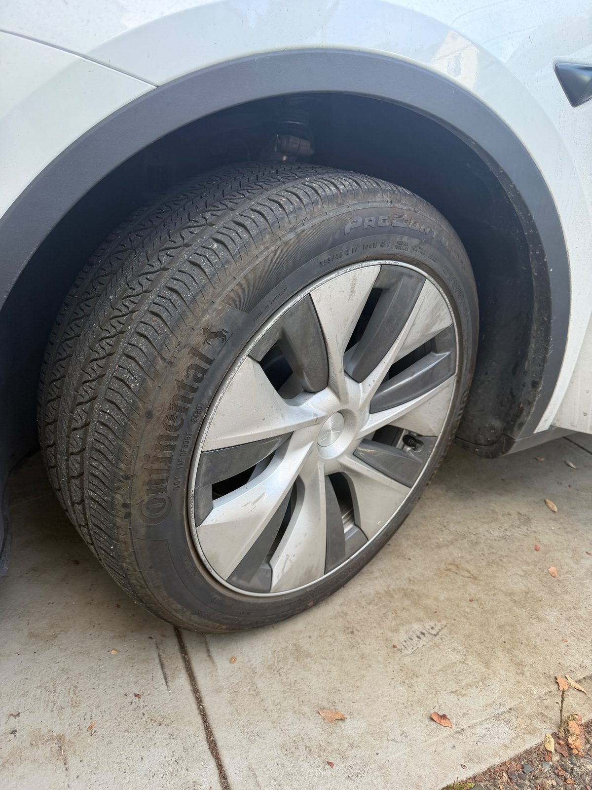 Front wheel of a white Tesla Model Y before detailing, with a brown film on the tyre and a grimy wheel cover