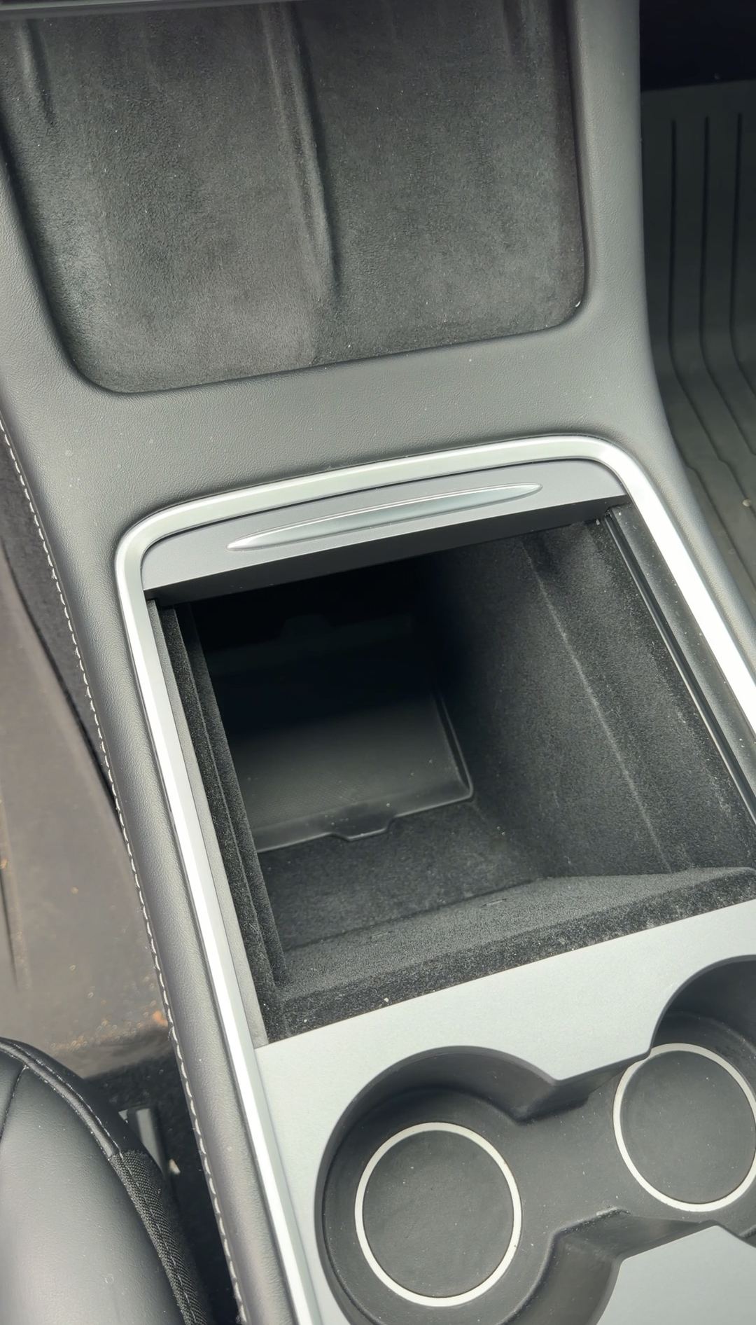 Open centre console storage bin of a Tesla Model Y before cleaning.