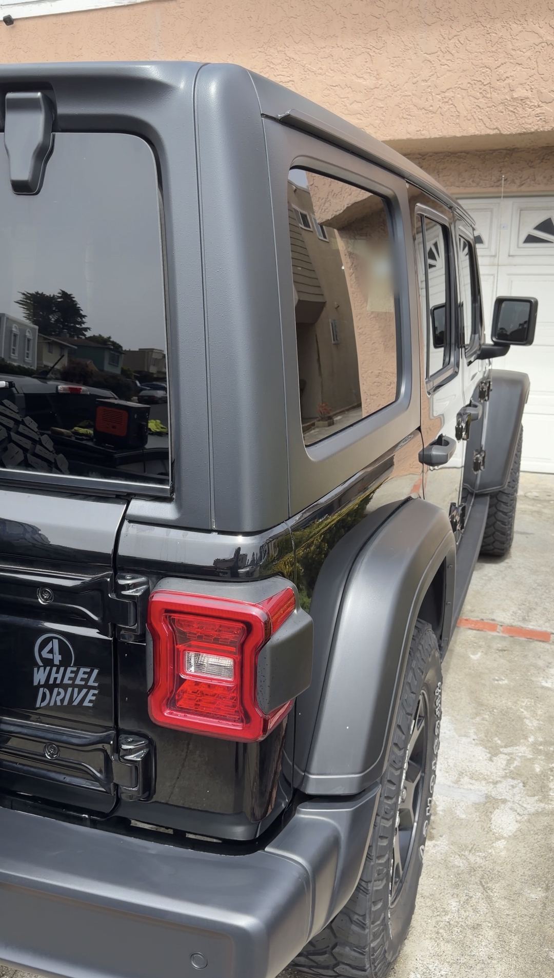 Clean black Jeep Wrangler rear quarter with 4 Wheel Drive decal on a wet driveway