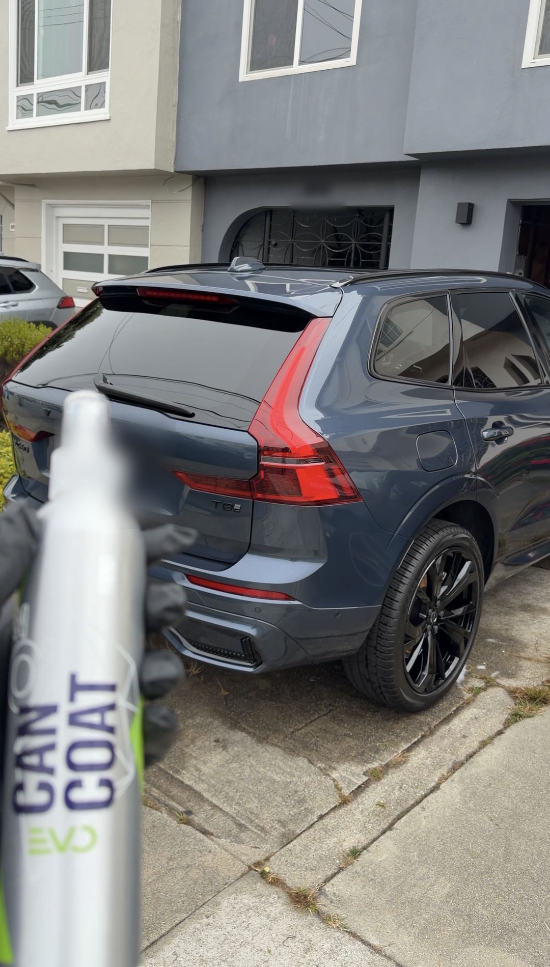 Gloved hand holding a CanCoat EVO spray bottle in front of a blue-grey Volvo XC60
