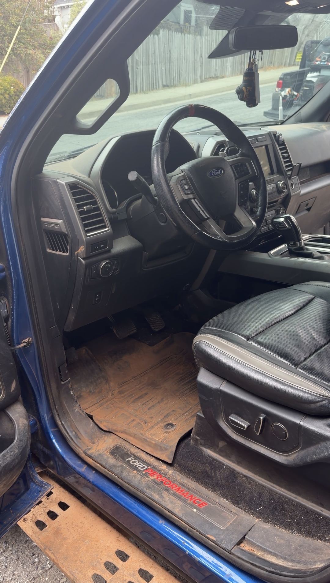 Driver's footwell of a Ford F-150 Raptor with a mud-caked floor liner before an interior detail