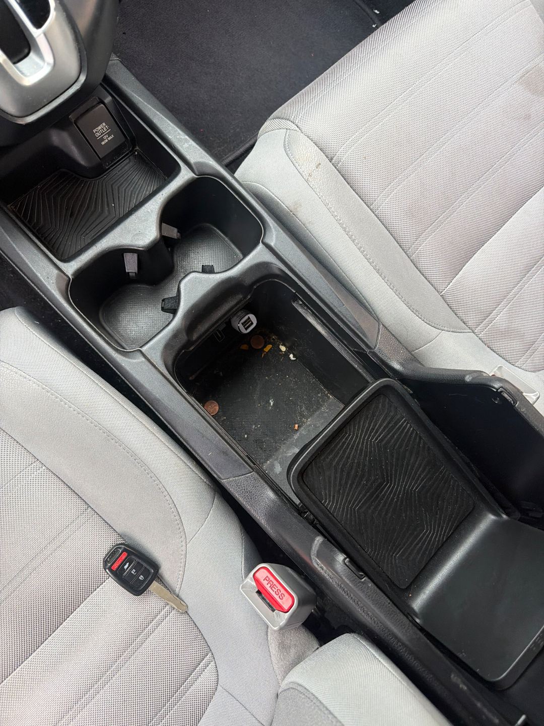 Centre console of a maroon Honda CR-V before detailing, its storage bin full of coins and crumbs