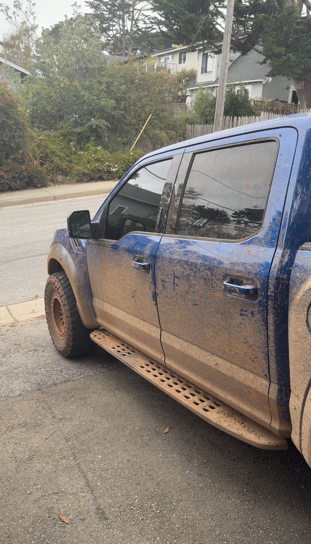Driver's side of a blue Ford F-150 Raptor sheeted in dried mud before a mobile detail