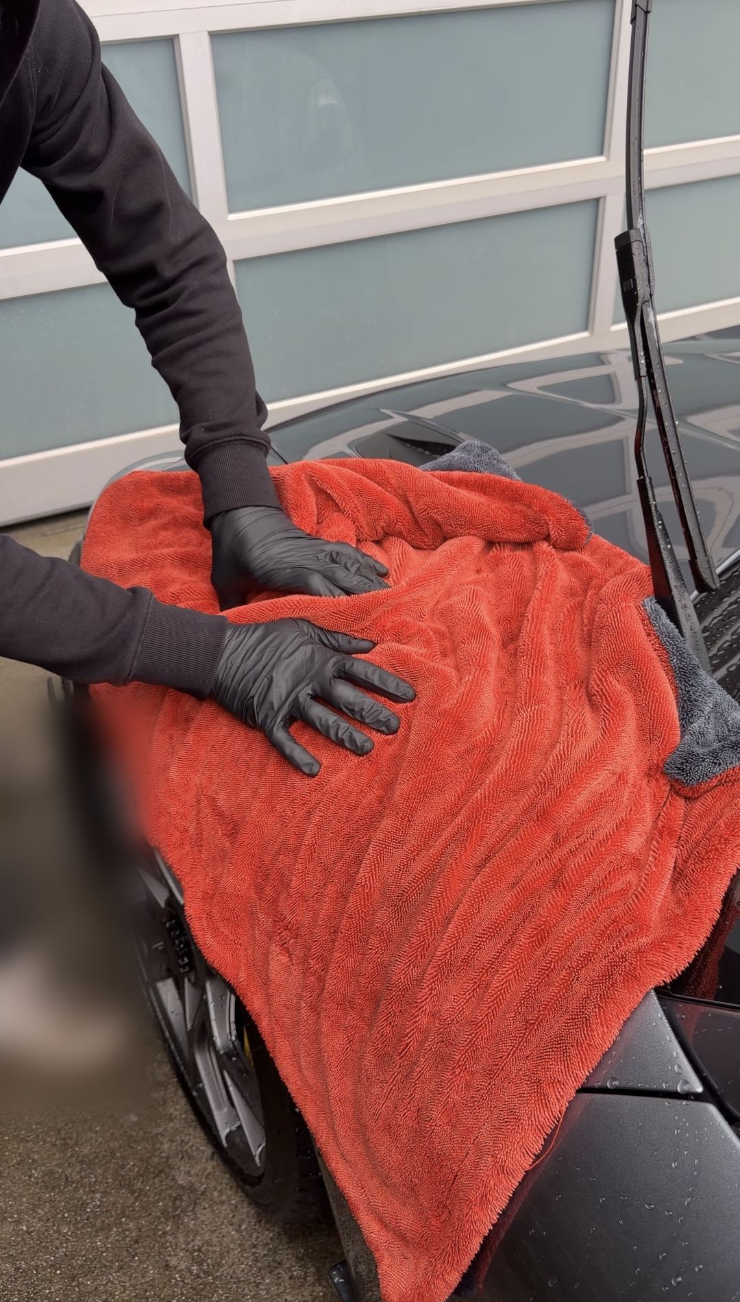 Detailer drying the bonnet of a grey Porsche 718 Spyder RS with a large orange microfibre towel.