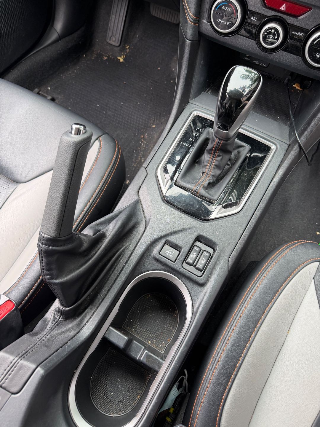 Centre console of a Subaru Crosstrek before detailing, with crumbs in the cupholders and dust on the trim