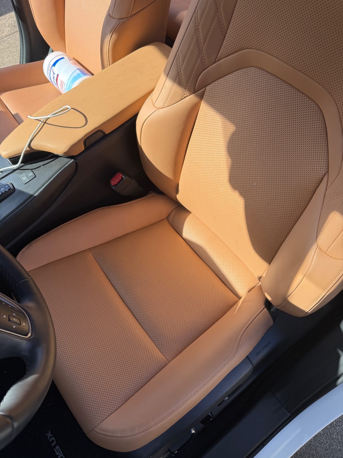 Front passenger seat of a white Lexus UX before detailing with a bottle and cord on the armrest