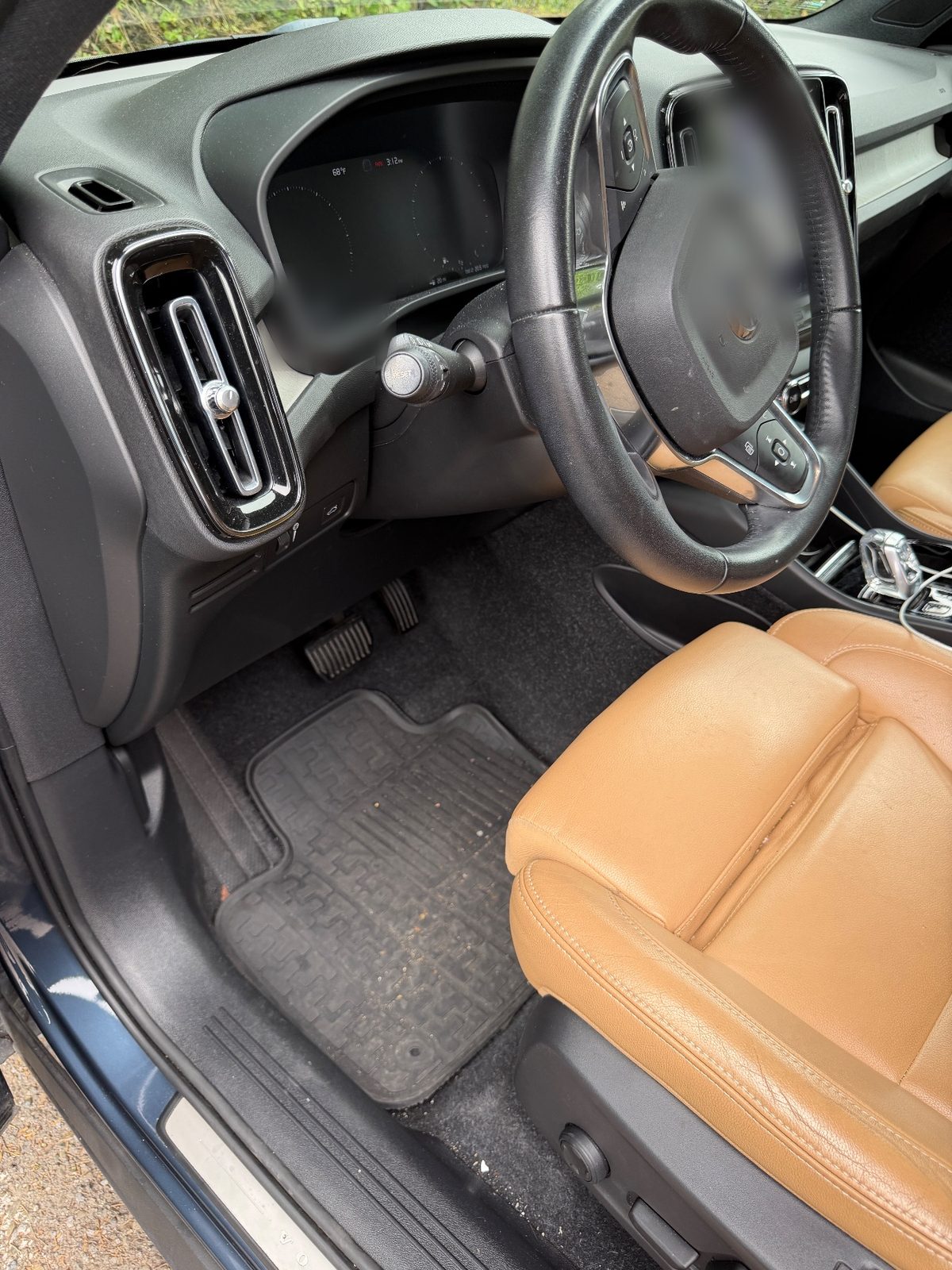 Driver footwell of a blue-grey Volvo XC40 before detailing, with grit and debris on the rubber mat
