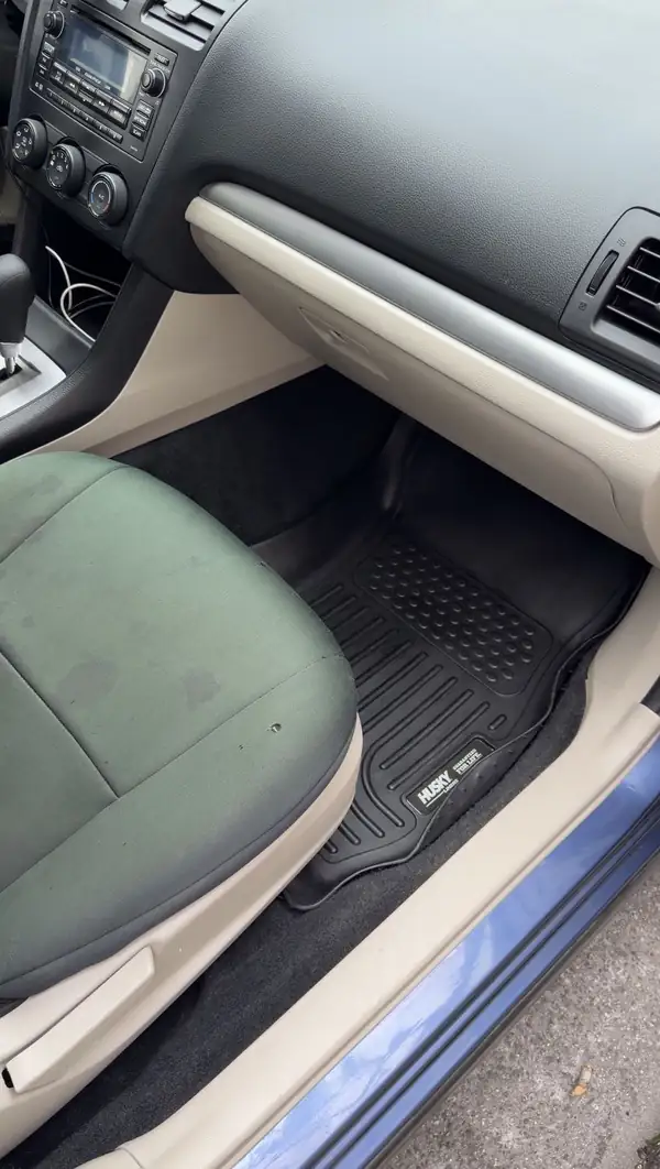 Clean front passenger footwell of a blue Subaru after detailing, the black rubber floor liner free of dirt.