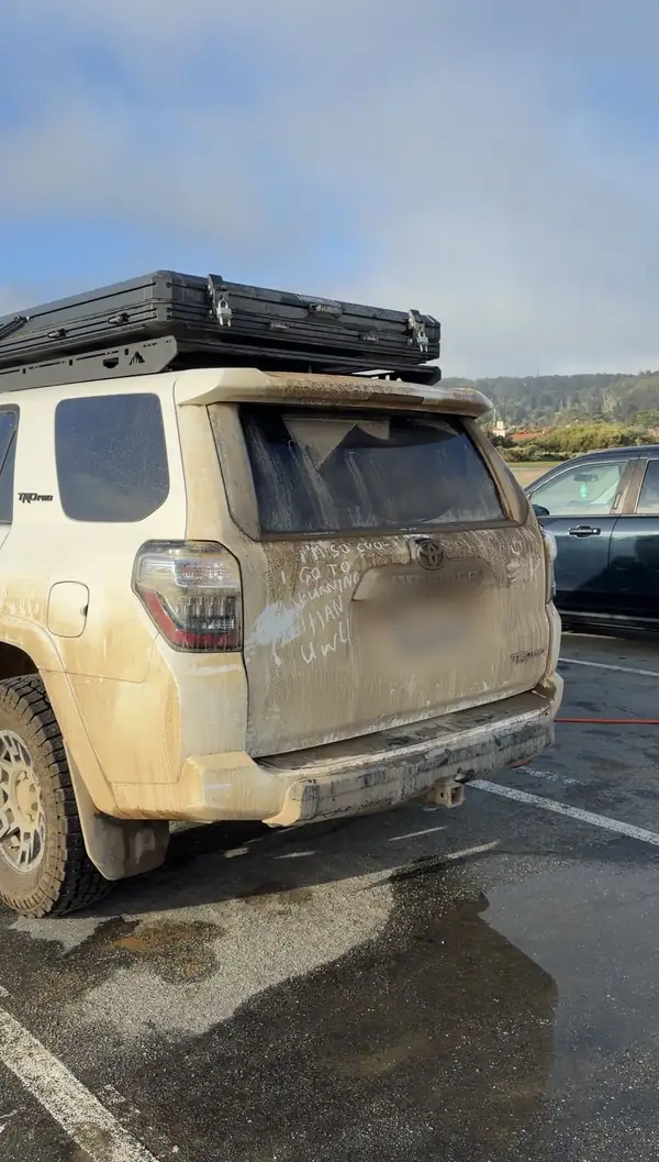 Rear of a mud-covered white Toyota 4Runner TRD Pro with a rooftop tent and writing in the dust on the tailgate
