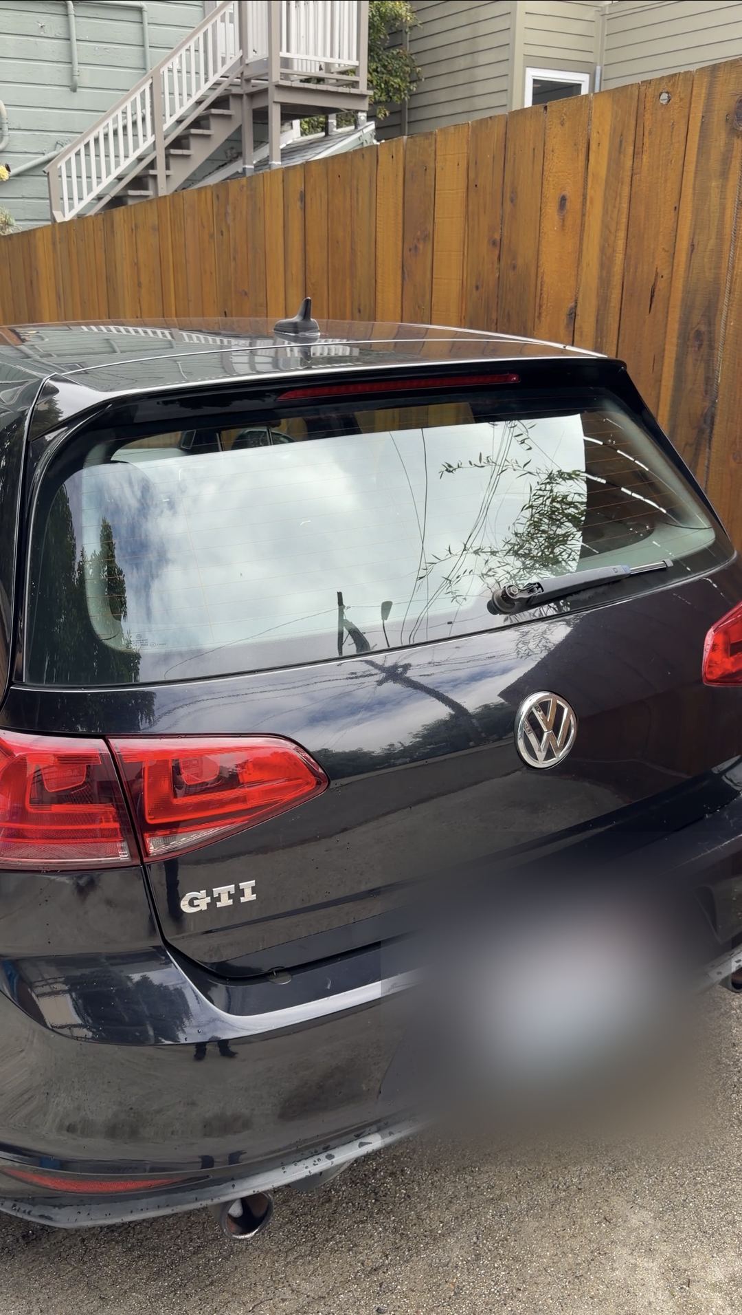 Rear of a black VW GTI parked in a driveway beside a wooden fence