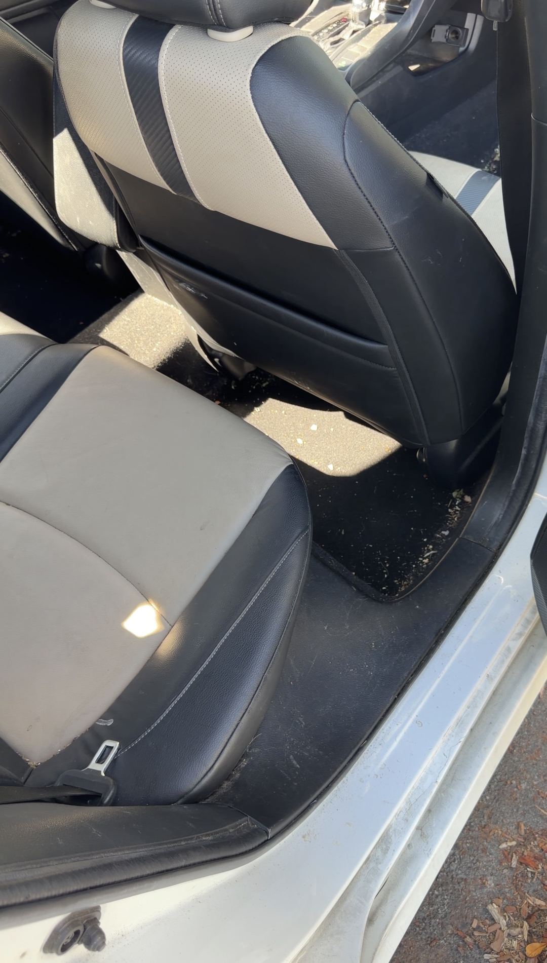 Rear driver-side seat and floor of a Honda Civic before cleaning, with crumbs on the cushion and grit on the mat