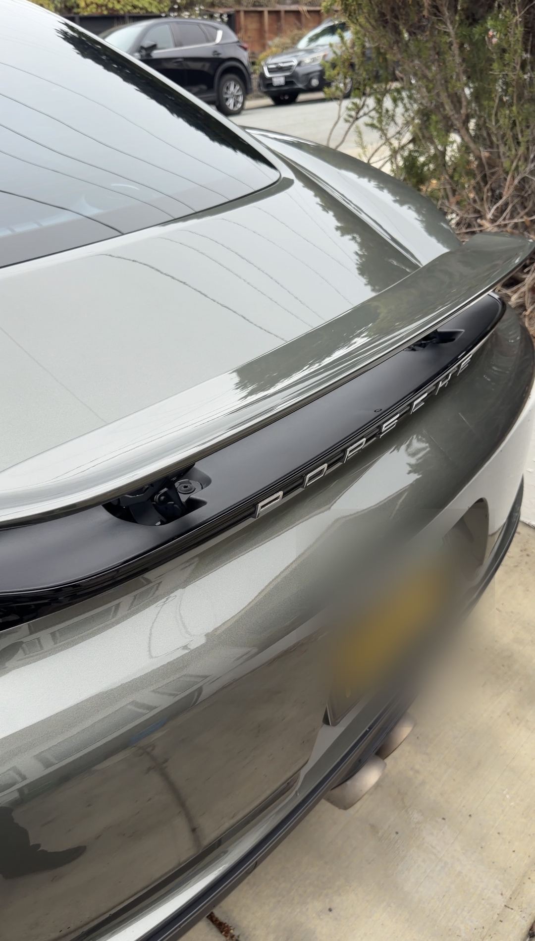 Clean rear deck and raised spoiler of a green Porsche 718 Cayman S after a mobile detail.