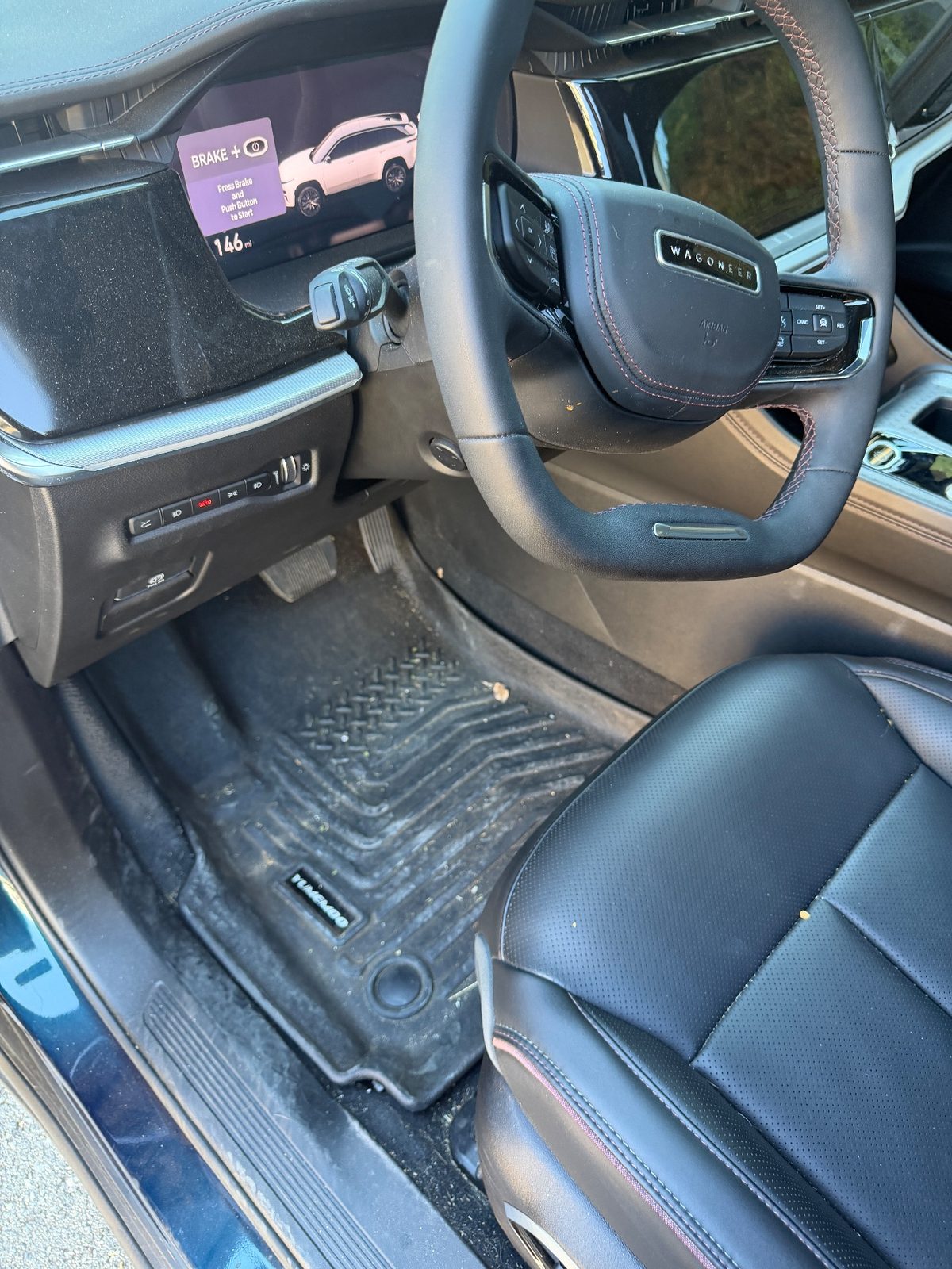 Driver footwell of a Jeep Wagoneer S before detailing, with dirt and debris on the floor mat