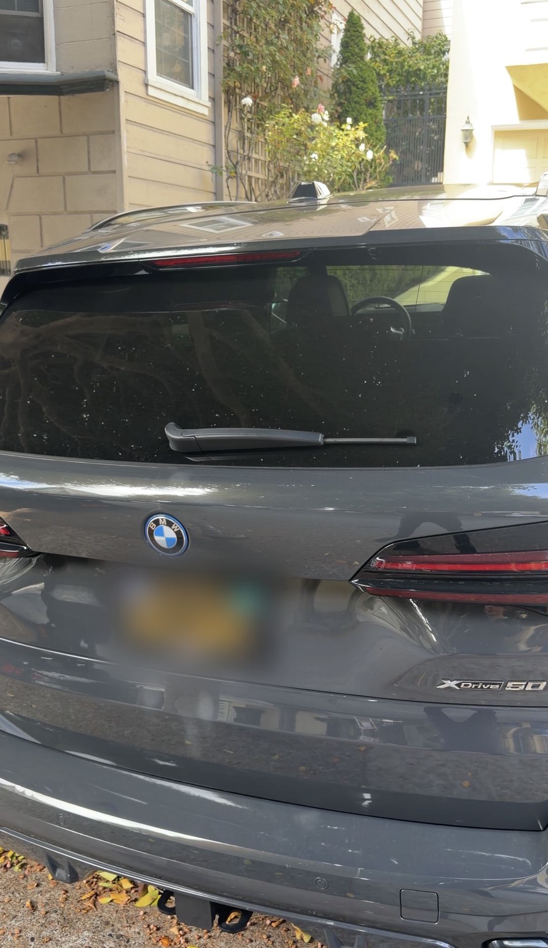 Rear tailgate of a dark grey BMW X5 before detailing, its rear glass covered in dried water spots and a dust film