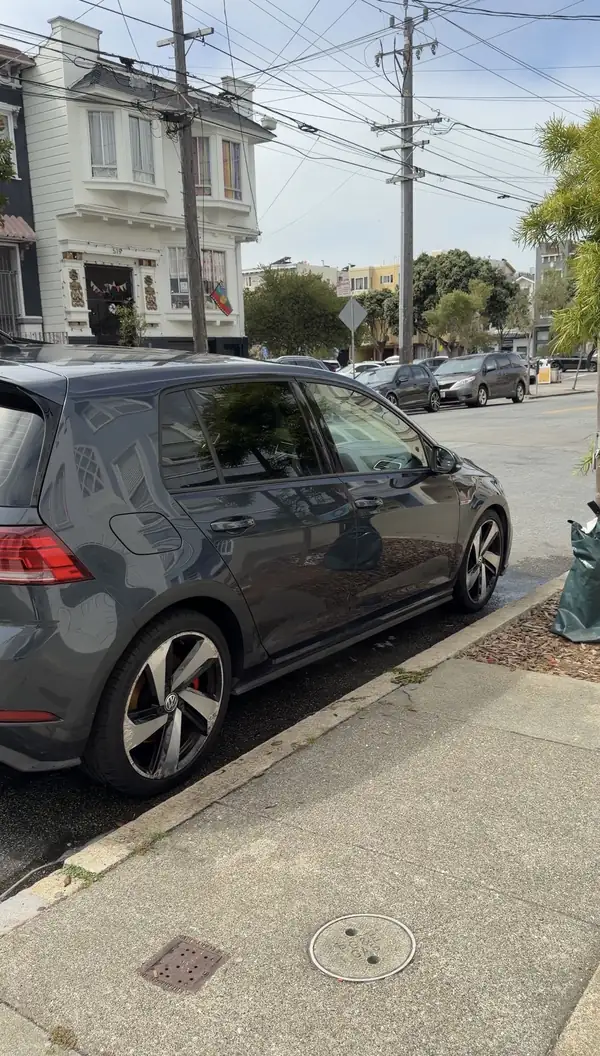 Dark grey Volkswagen Golf GTI parked at the kerb on a San Francisco street after a wash, paint reflecting the buildings opposite.