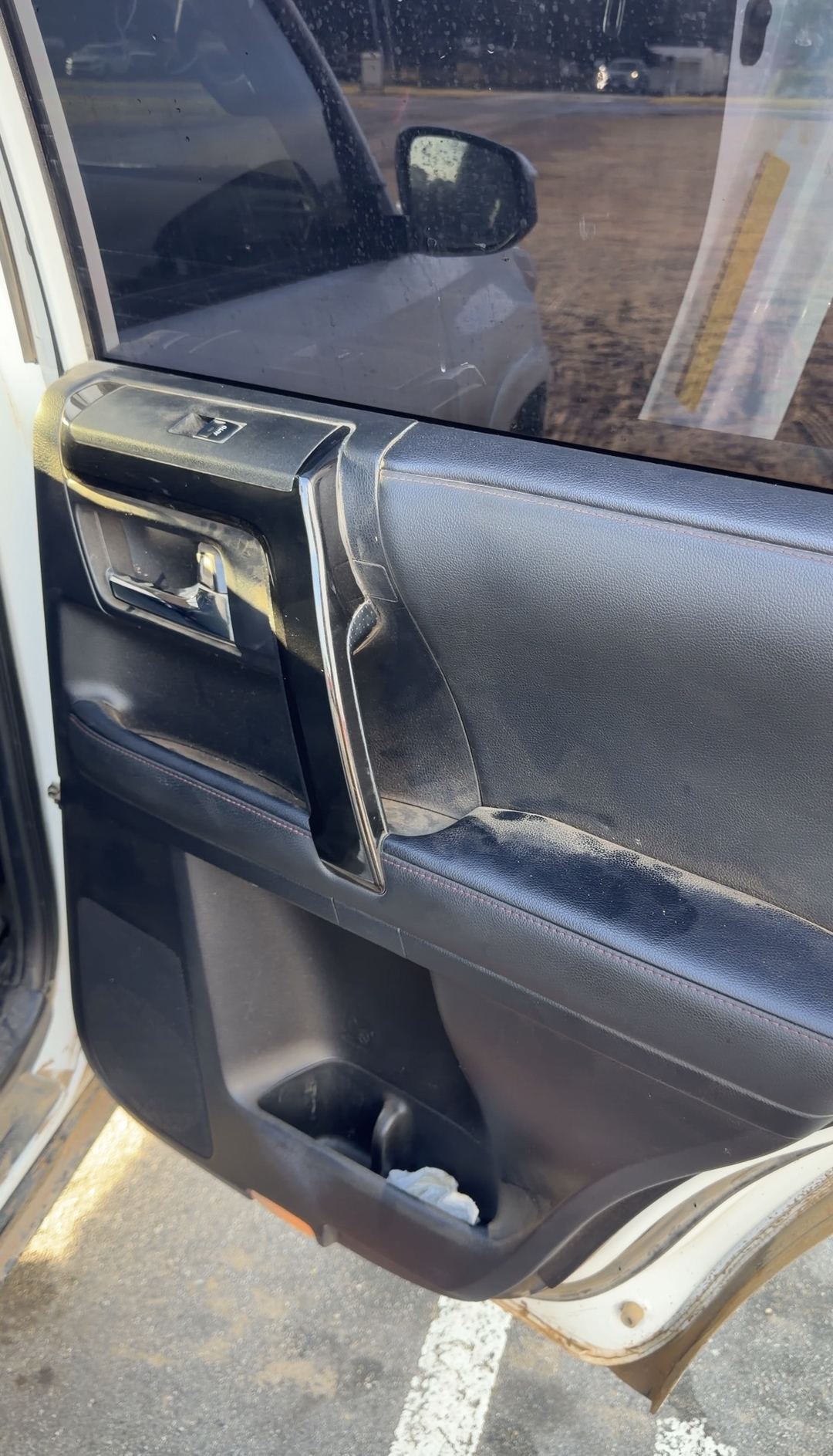 Rear door panel of a Toyota 4Runner with a dusty grab handle and armrest and a tissue in the door pocket