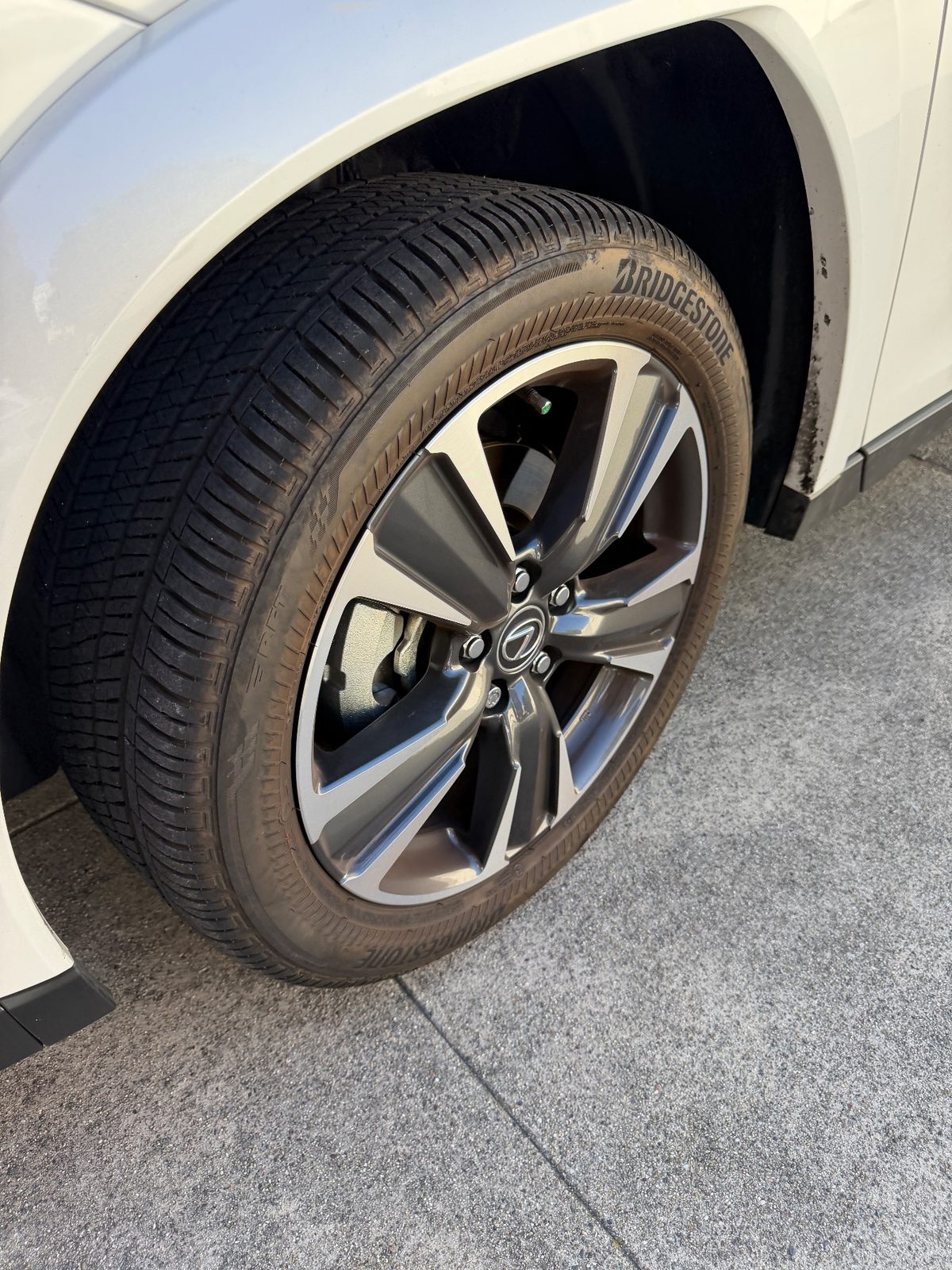 Alloy wheel of a white Lexus UX before cleaning with mud spatter on the arch