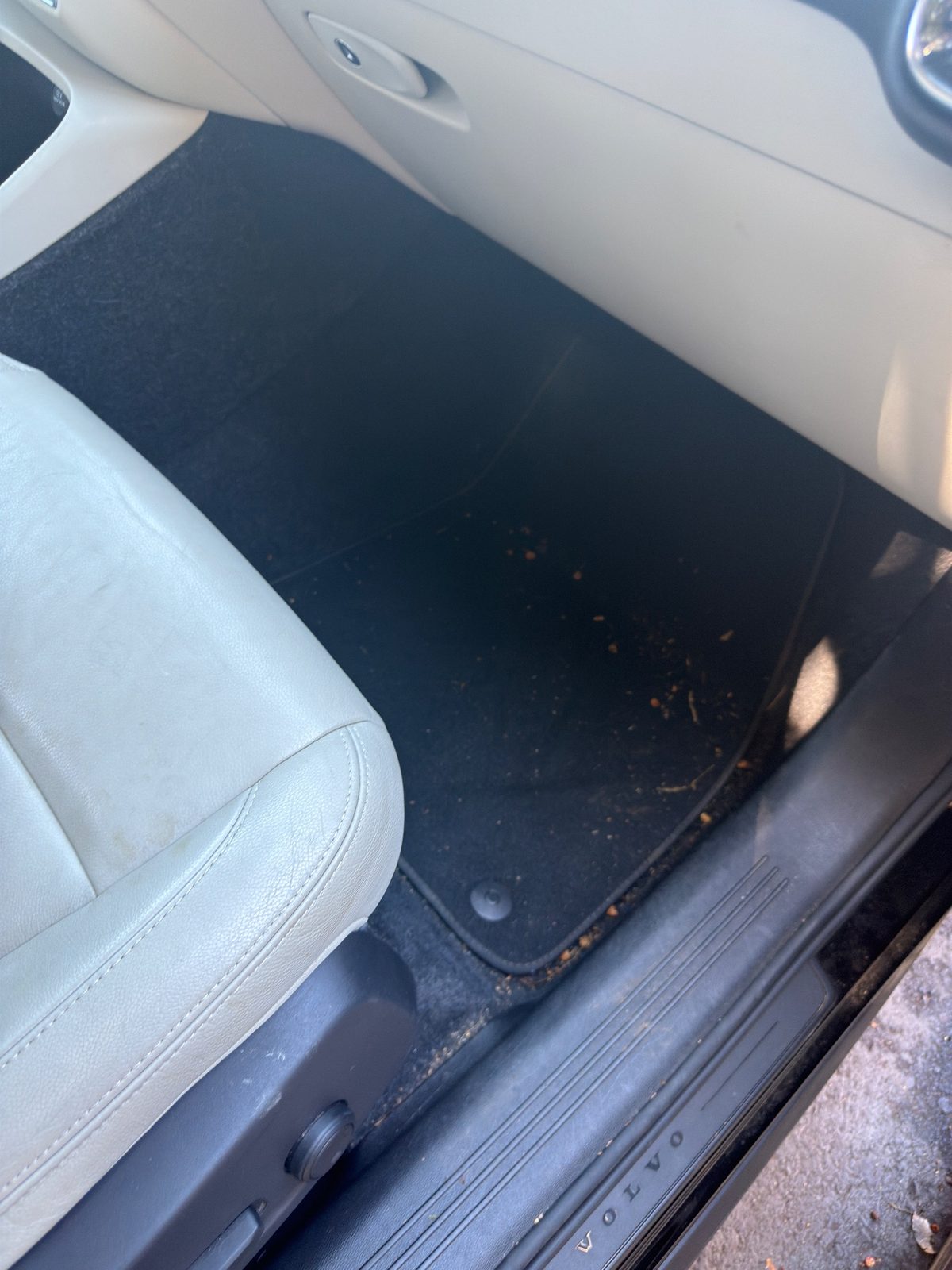 Front passenger footwell of a Volvo XC40 before detailing, with crumbs and debris scattered on the black mat