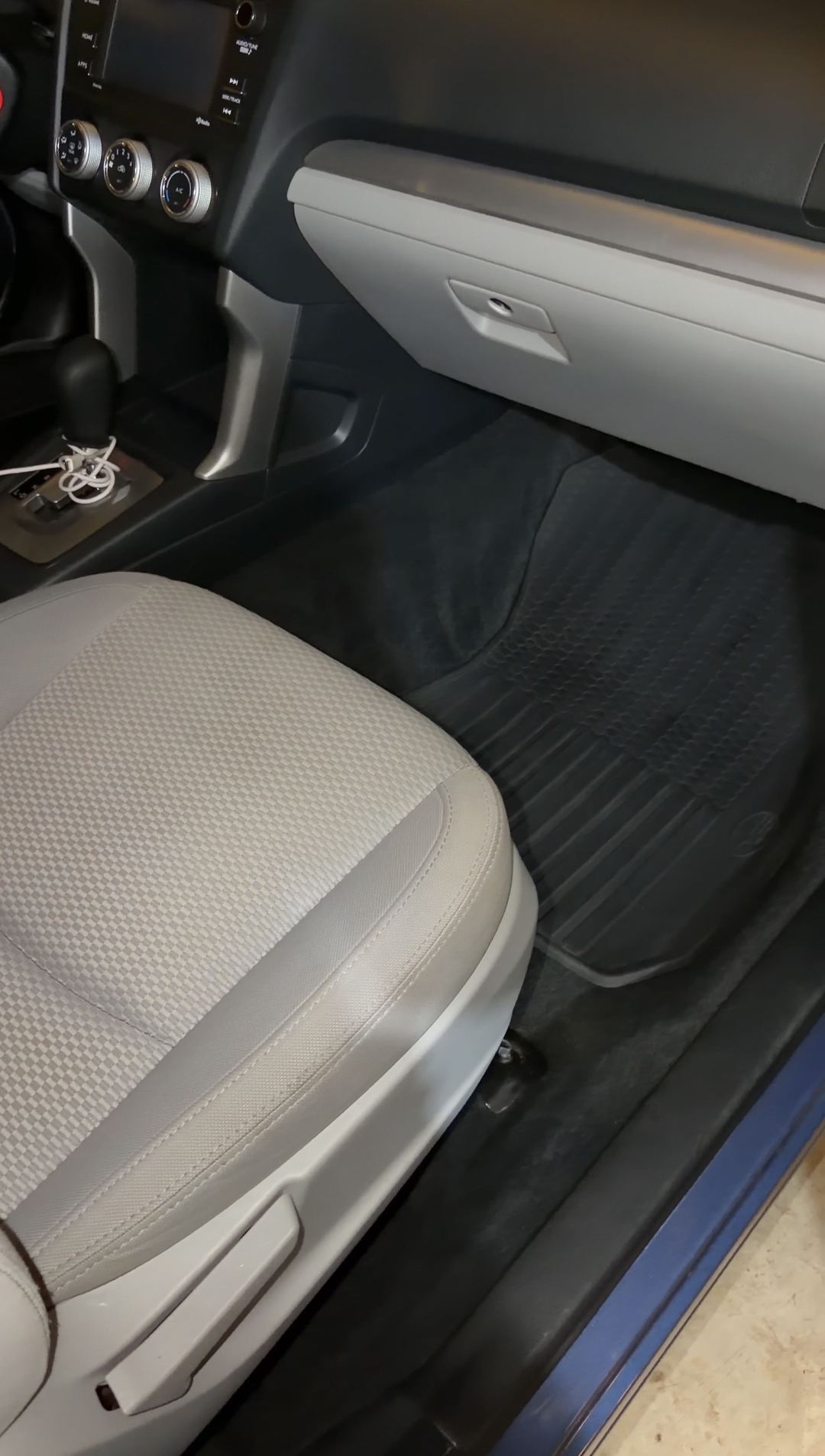 Front passenger footwell of a blue Subaru Forester after detailing, the black rubber all-weather mat clean beneath the grey glovebox.