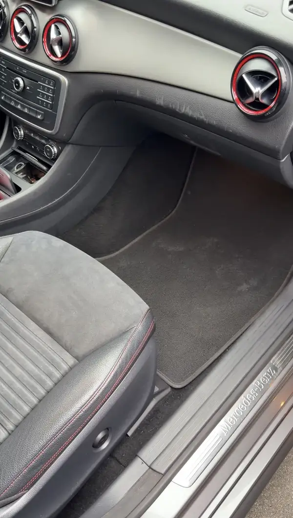 Dirty front passenger footwell of a grey Mercedes-Benz CLA250 before detailing, with a chalky pale deposit across the carpet mat