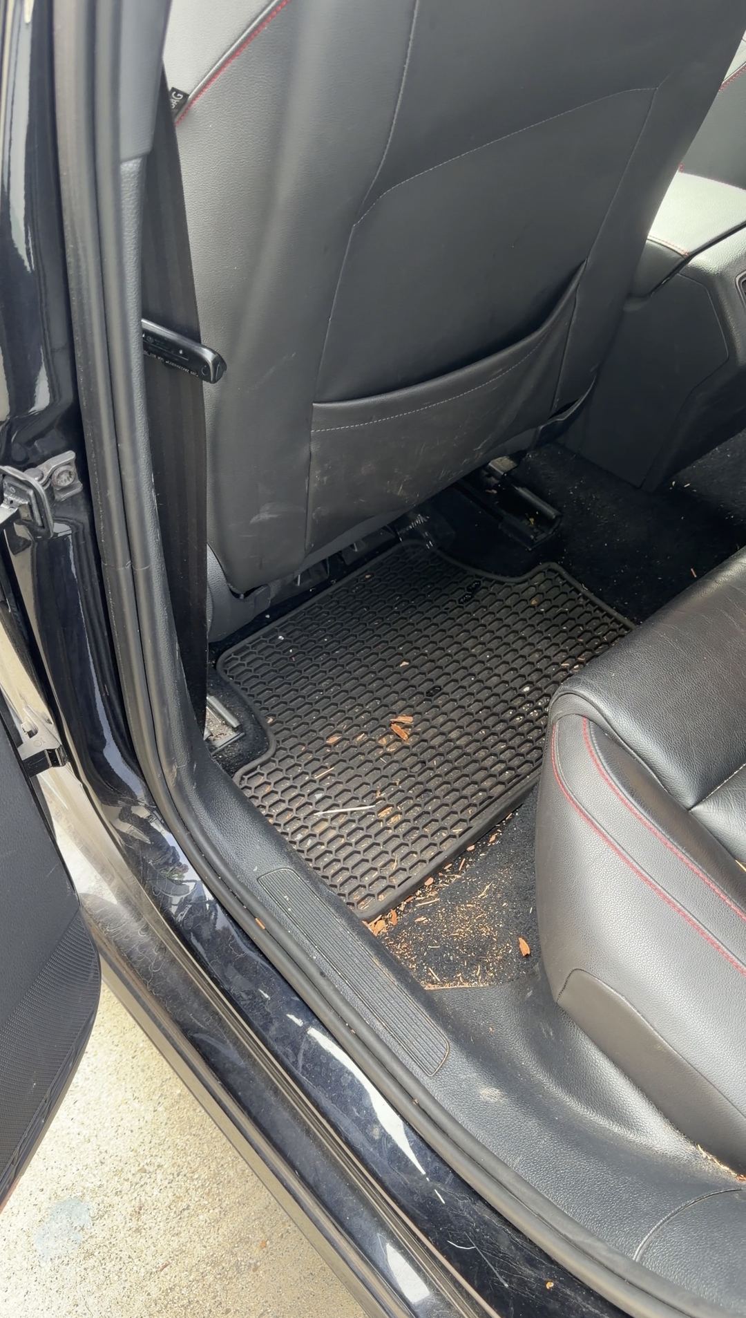 Rear footwell of a black VW GTI before cleaning, debris on the rubber mat