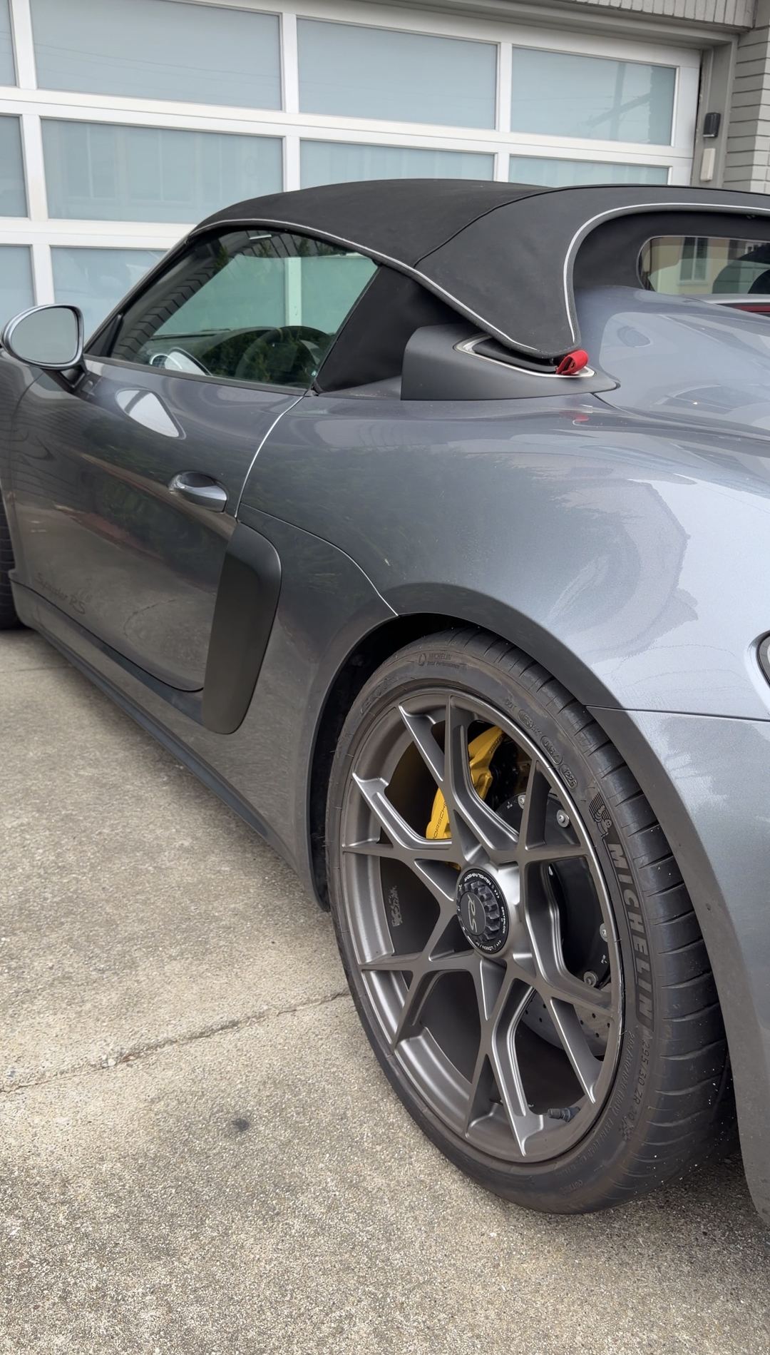 Driver's side of a grey Porsche 718 Spyder RS before washing, showing the Spyder RS sill script under a film of road dust.