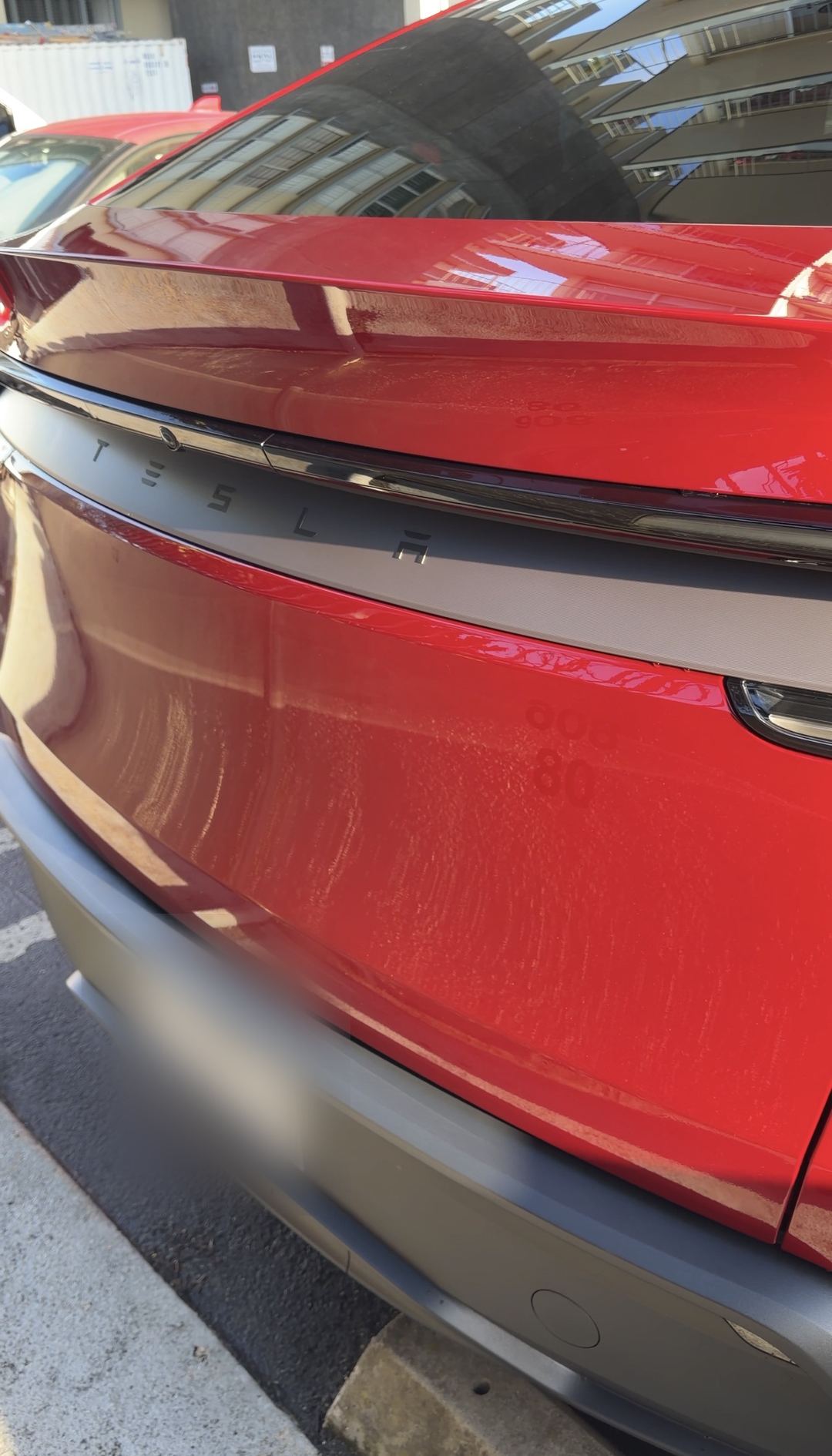 Clean red Tesla liftgate and badge reflecting a building after an exterior detail