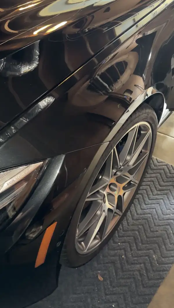 Forged wheel and blue M brake caliper on the mirror-black front fender of a detailed BMW M3
