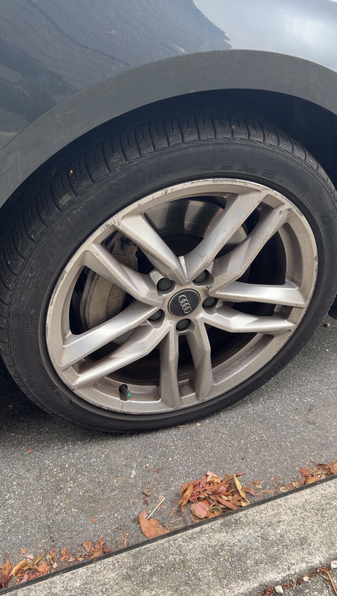 Brake dust on the twin five-spoke front alloy wheel of a grey Audi A4 parked at a curb