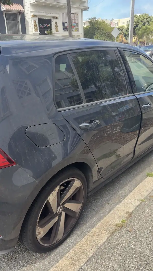 Passenger side rear quarter of a dark grey Volkswagen Golf GTI covered in dust before washing.