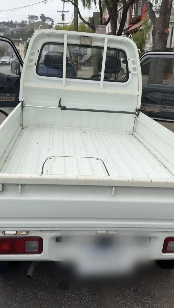 Rear view of a white Honda Acty kei truck with the tailgate dropped, showing the dirty cargo bed floor before cleaning.