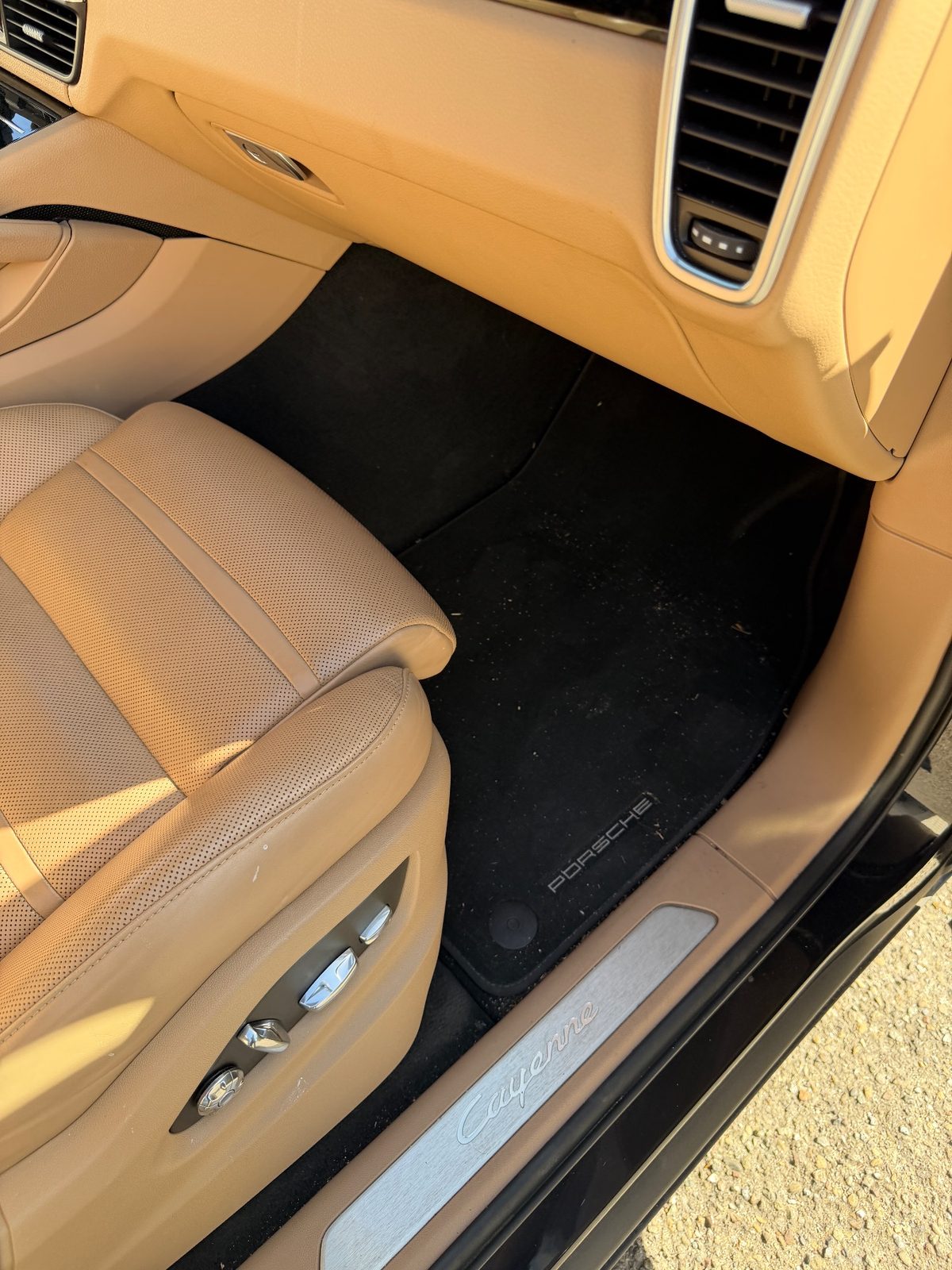 Passenger footwell of a dark blue Porsche Cayenne before cleaning, carpet mat covered in dust and debris