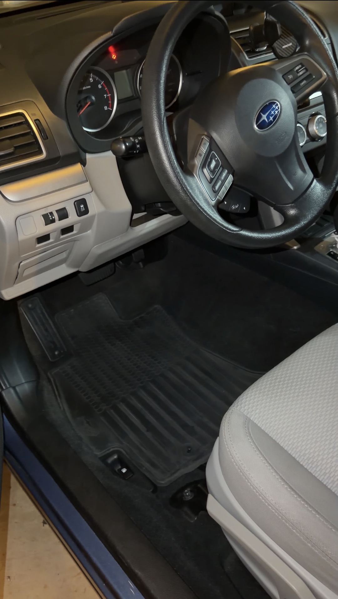Driver's footwell of a blue Subaru Forester after detailing, the black rubber all-weather mat clean and free of dust.