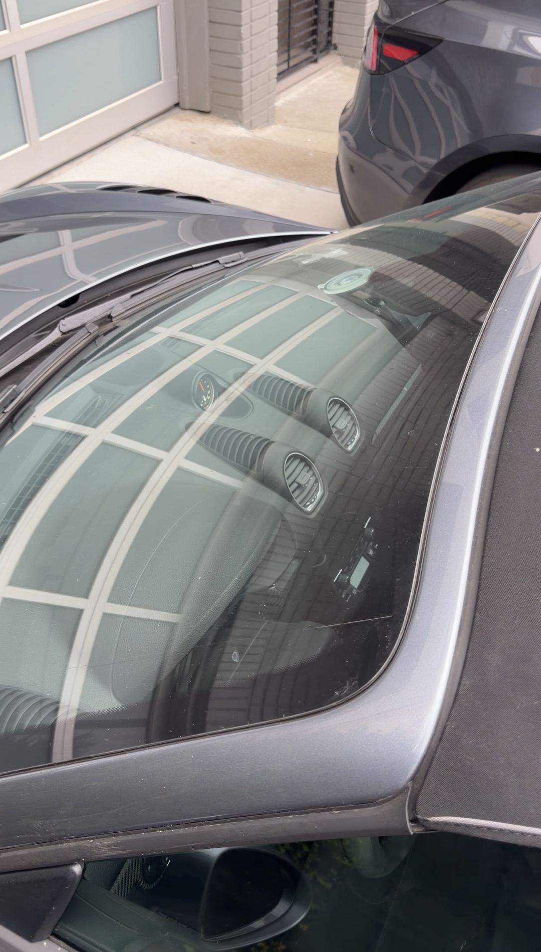 Windscreen and cowl of a grey Porsche 718 Spyder RS before cleaning, with the dashboard visible through the glass.