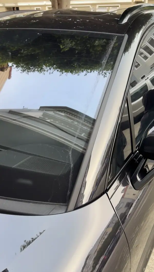 Dried streaks and specks on the windshield of a black Porsche Macan GTS before an exterior detail.