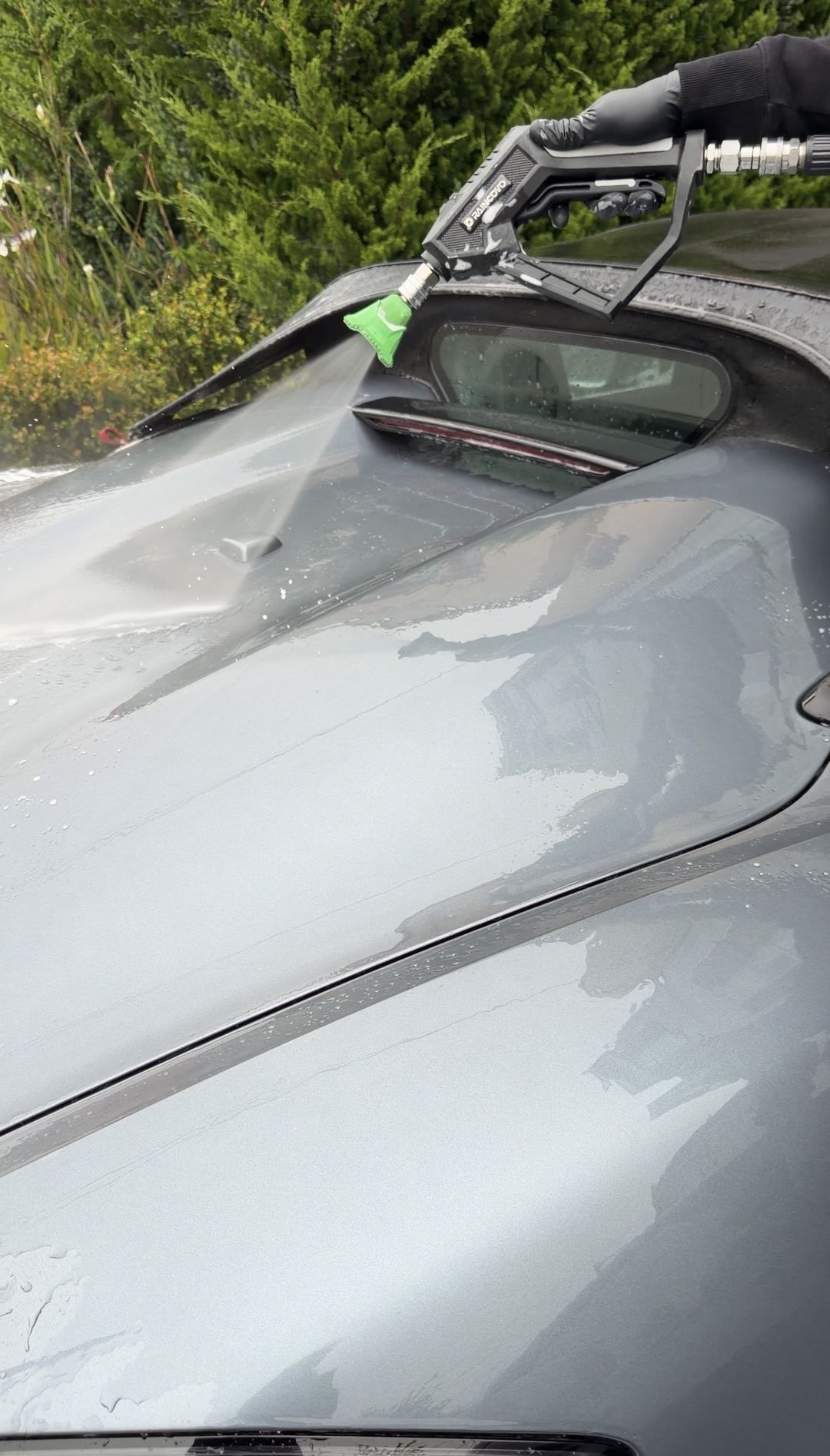 Pressure washer rinsing the rear deck of a grey Porsche 718 Spyder RS during a mobile detail.
